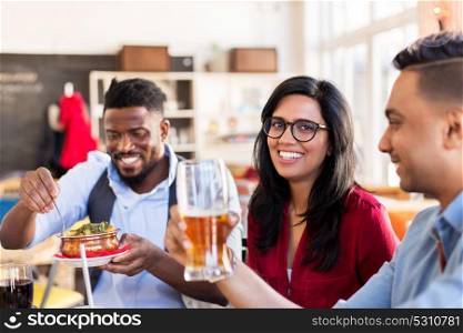 leisure, food and people concept - group of happy international friends eating and drinking at restaurant or bar. happy friends eating at restaurant