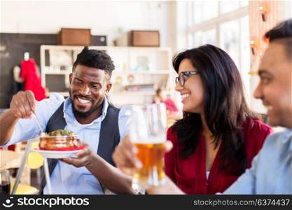 leisure, food and people concept - group of happy international friends eating and drinking at restaurant or bar. happy friends eating at restaurant