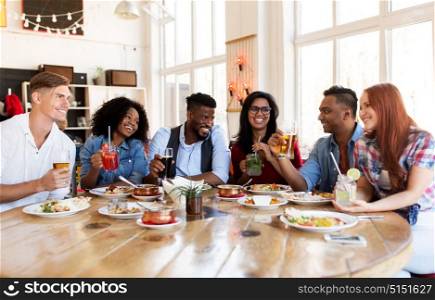 leisure, food and people concept - group of happy international friends with drinks eating and talking at restaurant table. happy friends eating and drinking at restaurant