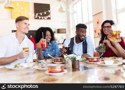 leisure, food and people concept - group of happy international friends with drinks eating and talking at restaurant table. happy friends eating and drinking at restaurant