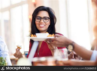 leisure, food and people concept - happy indian woman with friends eating at restaurant. happy indian woman eating at restaurant