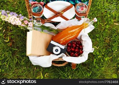 leisure, food and summer concept - close up of juice, cherry, book and camera in picnic basket. juice, cherry, book and camera in picnic basket