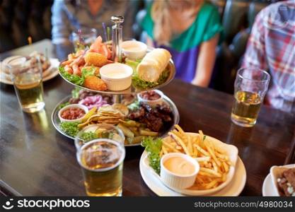 leisure, food, drinks and holidays concept - people sitting at table with food and beer glasses at bar or pub. people sitting at table with food and beer at bar