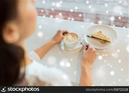 leisure, food, drinks, holidays people and lifestyle concept - close up of young woman hands eating cake and drinking coffee at cafe over snow effect