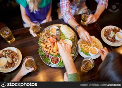 leisure, food, drinks, people and holidays concept - friends eating snack and drinking beer at bar or pub. friends eating and drinking at bar or pub