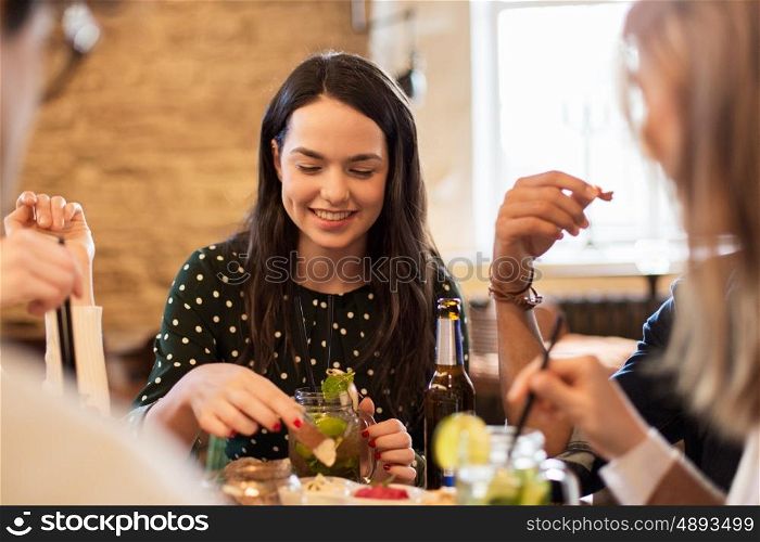 leisure, food, drinks, people and holidays concept - happy friends eating and drinking at bar or cafe
