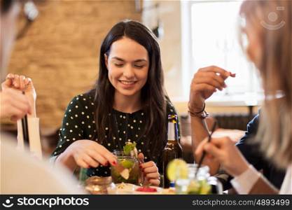 leisure, food, drinks, people and holidays concept - happy friends eating and drinking at bar or cafe