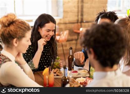 leisure, food, drinks, people and holidays concept - happy friends eating and drinking at bar or cafe. happy friends eating and drinking at bar or cafe