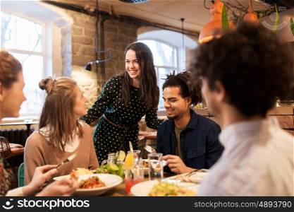 leisure, food, drinks, people and holidays concept - happy friends eating and drinking at restaurant