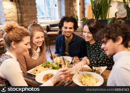 leisure, food, drinks, people and holidays concept - happy friends with smartphone eating and drinking at restaurant