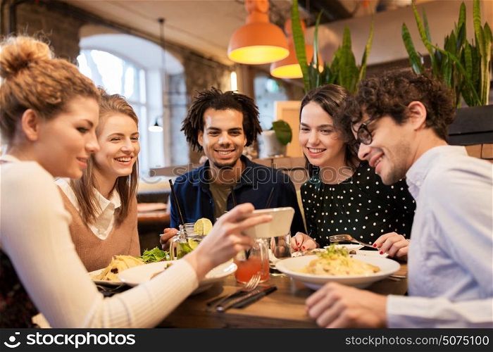 leisure, food, drinks, people and holidays concept - happy friends with smartphone eating and drinking at restaurant. friends with smartphone eating at restaurant