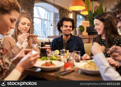 leisure, food, drinks, people and holidays concept - happy friends with smartphones eating and drinking at restaurant. friends with smartphones eating at restaurant