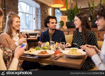 leisure, food, drinks, people and holidays concept - happy friends with smartphones eating and drinking at restaurant. friends with smartphones eating at restaurant