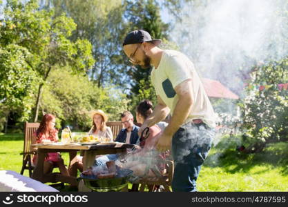 leisure, food, people and holidays concept - man cooking meat on barbecue grill for his friends at summer outdoor party