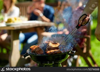leisure, food, people and holidays concept - man cooking meat on barbecue grill for his friends at summer outdoor party. man cooking meat on barbecue grill at summer party