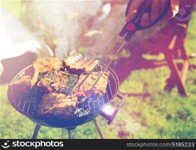 leisure, food, people and holidays concept - man cooking meat on barbecue grill at outdoor summer party. man cooking meat on barbecue grill at summer party