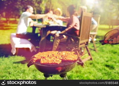 leisure, food, people and holidays concept - man cooking meat on barbecue grill for his friends at summer outdoor party. man cooking meat on barbecue grill at summer party