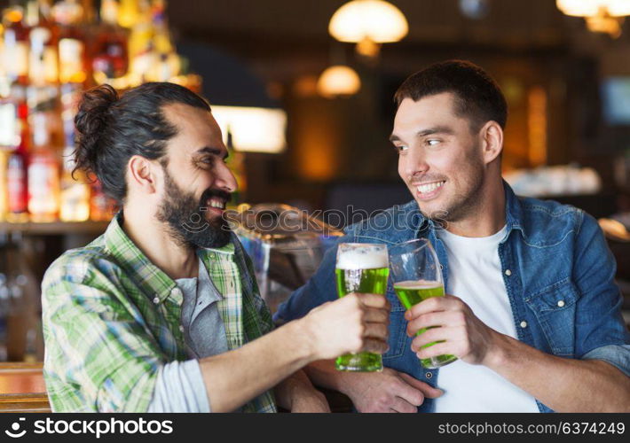 leisure, friendship, st patricks day and celebration concept - happy male friends drinking green beer and clinking glasses at bar or pub. male friends drinking green beer at bar or pub