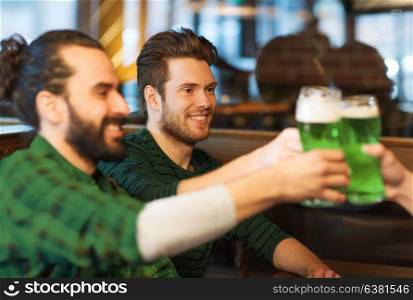 leisure, friendship, st patricks day and celebration concept - happy male friends drinking green beer and clinking glasses at bar or pub. male friends drinking green beer at bar or pub