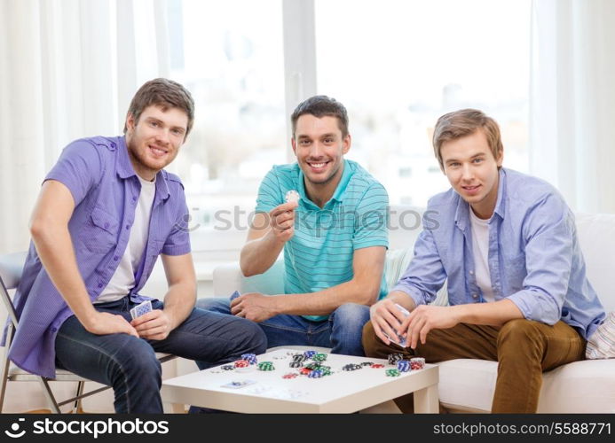 leisure, games and lifestyle concept - happy three male friends playing poker at home