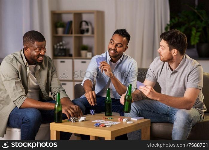 leisure games, friendship and gambling concept - happy male friends playing cards and drinking beer at home at night. happy male friends playing cards at home at night