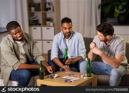 leisure games, friendship and gambling concept - happy male friends playing cards and drinking beer at home at night. happy male friends playing cards at home at night