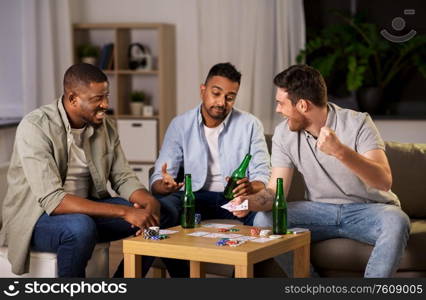 leisure games, friendship and gambling concept - male friends playing cards and drinking beer at home at night. male friends playing cards at home at night