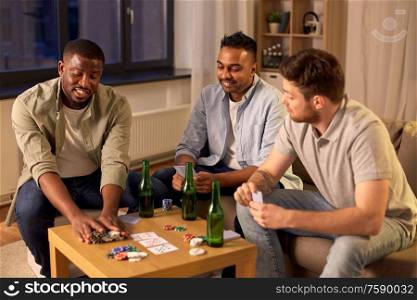 leisure games, friendship and gambling - male friends playing cards and drinking beer at home at night. smiling male friends playing cards at home