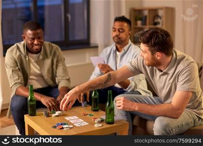 leisure games, friendship and gambling - male friends playing cards and drinking beer at home at night. smiling male friends playing cards at home