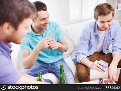 leisure, games, friendship, gambling and entertainment - three smiling male friends playing cards and drinking beer at home
