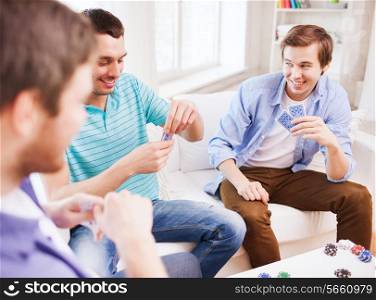 leisure, games, friendship, gambling and entertainment - three smiling male friends playing cards at home
