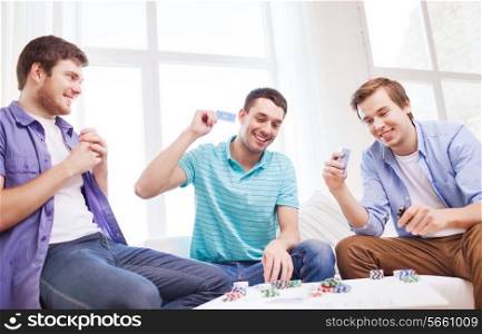 leisure, games, friendship, gambling and entertainment - three smiling male friends playing cards at home