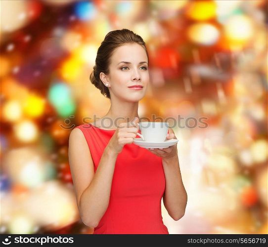 leisure, happiness, holidays and drink concept - smiling woman in red dress with cup of coffee over shiny lights background