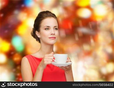 leisure, happiness, holidays and drink concept - smiling woman in red dress with cup of coffee over shiny lights background
