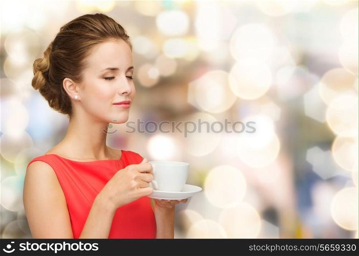 leisure, happiness, holidays and drink concept - smiling woman in red dress with closed eyes holding cup of coffee over shiny lights background