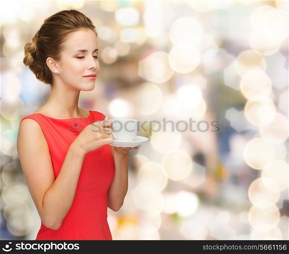 leisure, happiness, holidays and drink concept - smiling woman in red dress with closed eyes holding cup of coffee over shiny lights background