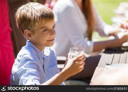 leisure, holidays and people concept - happy boy with glass of water at family dinner summer party. happy boy with glass of water at festive dinner
