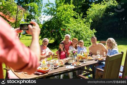 leisure, holidays and people concept - happy family having festive dinner or summer garden party and photographing by smartphone. happy family photographing by smartphone in summer