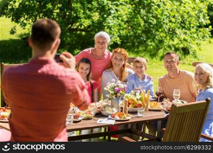 leisure, holidays and people concept - happy family having festive dinner or summer garden party and photographing by smartphone. happy family photographing by smartphone in summer