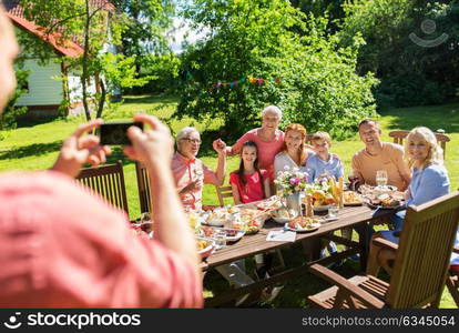 leisure, holidays and people concept - happy family having festive dinner or summer garden party and photographing by smartphone. happy family photographing by smartphone in summer