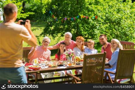 leisure, holidays and people concept - happy family having festive dinner or summer garden party and photographing by smartphone. happy family photographing at dinner in garden