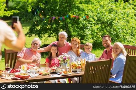 leisure, holidays and people concept - happy family having festive dinner or summer garden party and photographing by smartphone. happy family photographing at dinner in garden. happy family photographing at dinner in garden