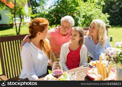 leisure, holidays and people concept - happy female family having festive dinner at summer garden and talking. happy family having dinner at summer garden