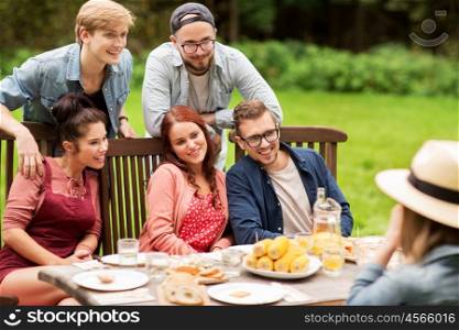 leisure, holidays, eating, people and food concept - happy friends having dinner and photographing at summer garden party