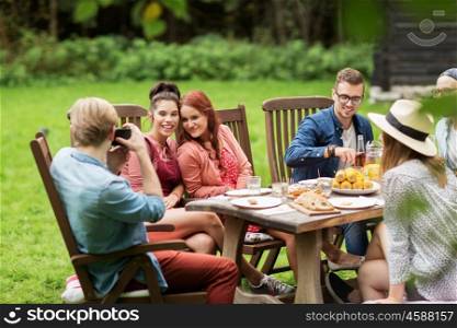 leisure, holidays, eating, people and food concept - happy friends having dinner and photographing at summer garden party