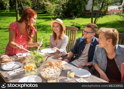 leisure, holidays, eating, people and food concept - happy friends having dinner and sharing salad at summer garden party