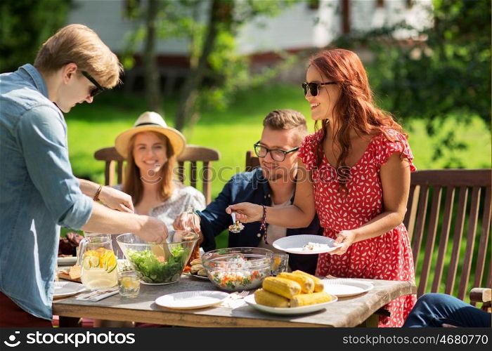 leisure, holidays, eating, people and food concept - happy friends having dinner and sharing salad at summer garden party