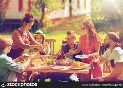 leisure, holidays, eating, people and food concept - happy friends having dinner and sharing salad at summer garden party. happy friends having dinner at summer garden party