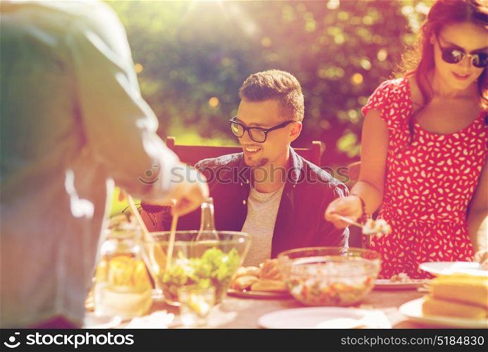 leisure, holidays, eating, people and food concept - happy friends having dinner and sharing salad at summer garden party. happy friends having dinner at summer garden party