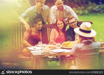 leisure, holidays, eating, people and food concept - happy friends having dinner and photographing at summer garden party. happy friends having dinner at summer garden party